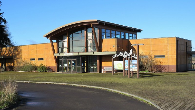Visitor Center at Tualatin River National Wildlife Refuge. The center is a golden brown building with a glassed entry with a high glass atrium and an arching roof.
