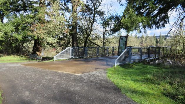 River overlook with concrete surface and gray fencing overlooking the Tualatin River, with trees alongside and in distance.